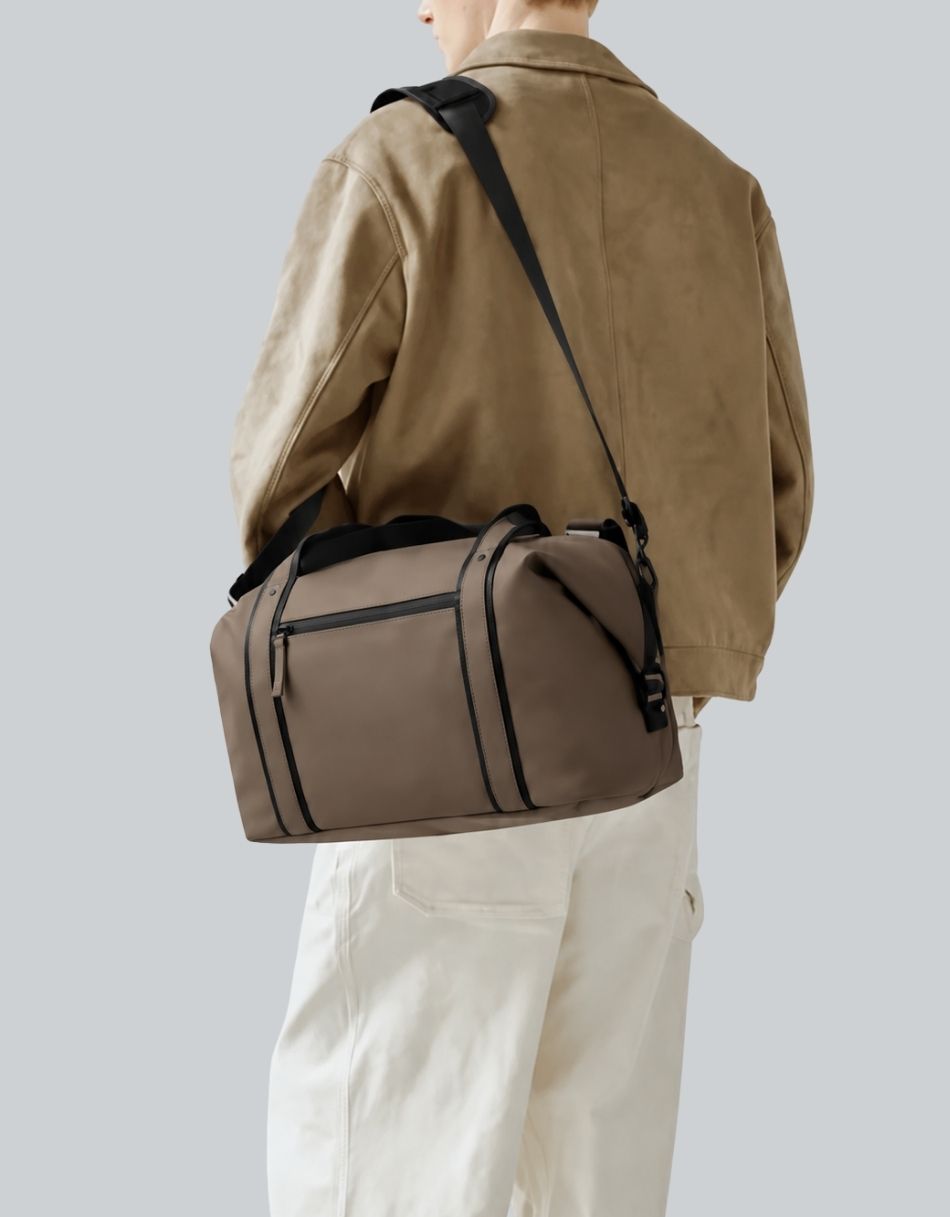 Modelo con bolso de viaje café Gaston Luga al hombro, con asas negras y bolsillo frontal
